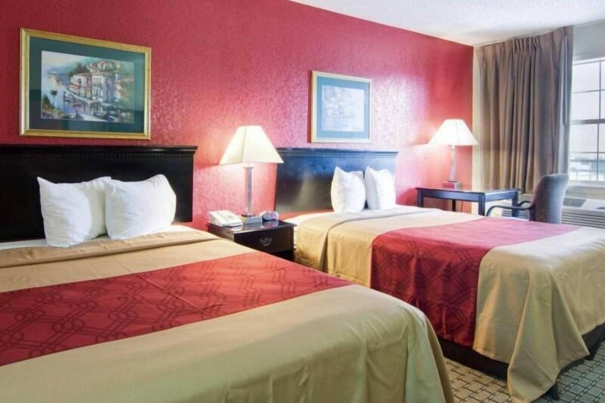 A hotel room with two beds, a desk, two lamps, and two paintings on the wall.