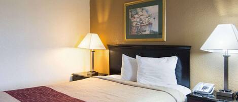 A hotel room with a bed, two bedside tables, a lamp, a painting on the wall, and a telephone on the nightstand.