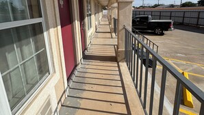 A covered corridor with doors, a parking area, and a clear sky. - Villa West Inn (Odessa)