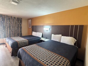 Een hotelkamer met twee bedden, een nachtkastje, een telefoon aan de muur en een gordijn met patroon.