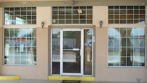 A building facade with a large glass door entrance, a neon 'OPEN' sign, and a yellow curb. - Villa West Inn (Odessa)
