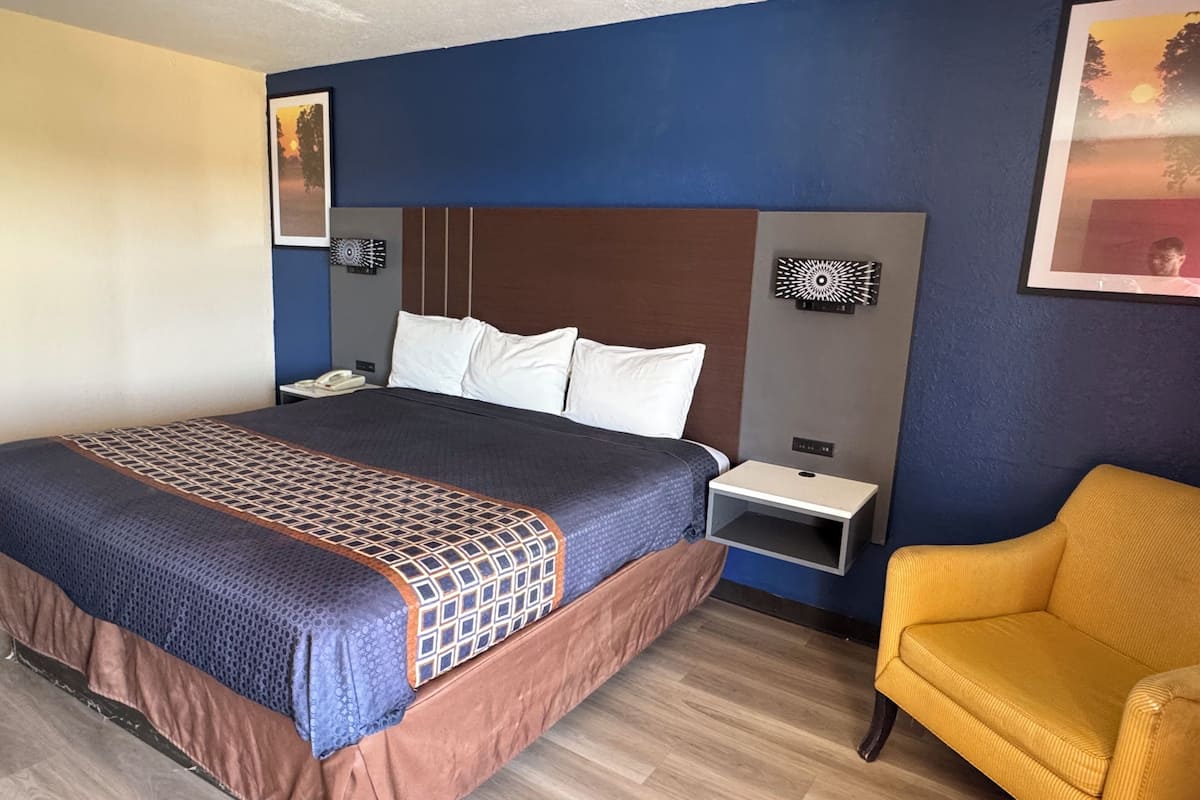 Ein Hotelzimmer mit einem großen Bett, einem Nachttisch, einem Sessel und einem an der Wand montierten Fernseher.