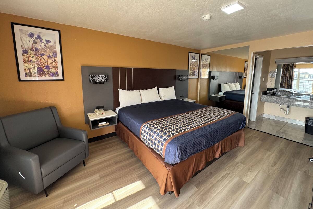 Ein Hotelzimmer mit einem Bett, einem Schlafsofa, einem Schreibtisch mit Telefon, einem Spiegel und einem durchgegangenen Tür angedeuteten Badezimmer.