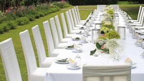 Een lange eettafel buiten, met witte stoelen, elk met een groene streep.