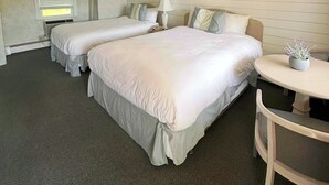 Een hotelkamer met twee bedden, een ronde spiegel, een klein tafeltje en een stoel.