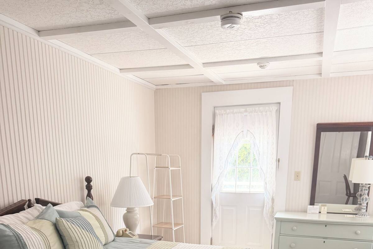 Un dormitorio con cama, mesita de noche, lámpara, cómoda y ventana con cortinas.