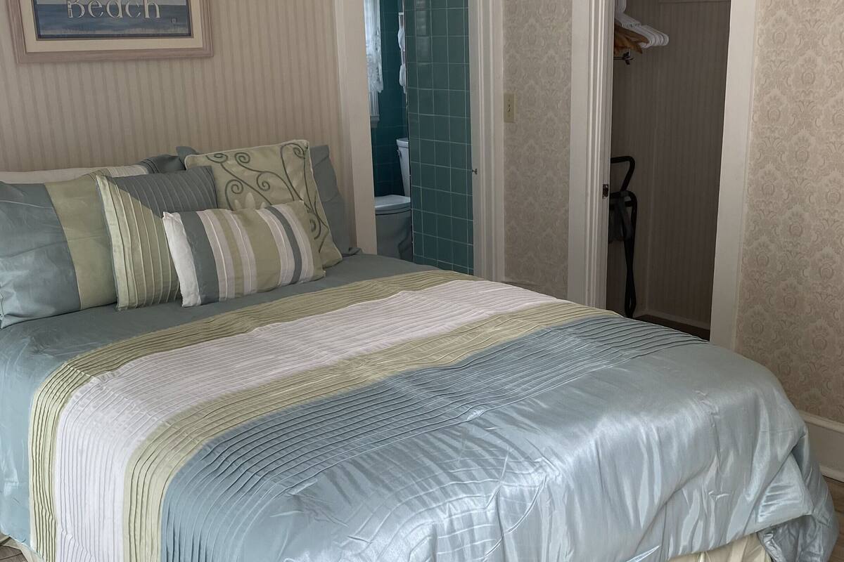 Un dormitorio con una cama, un cuadro en la pared y un baño visible a través de una puerta abierta.