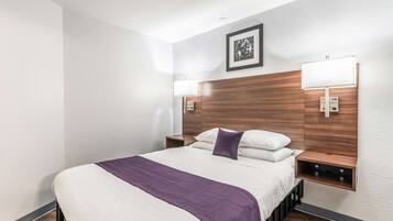 A hotel room with a large bed, two bedside tables, a wall-mounted lamp, and a framed picture above the bed.
