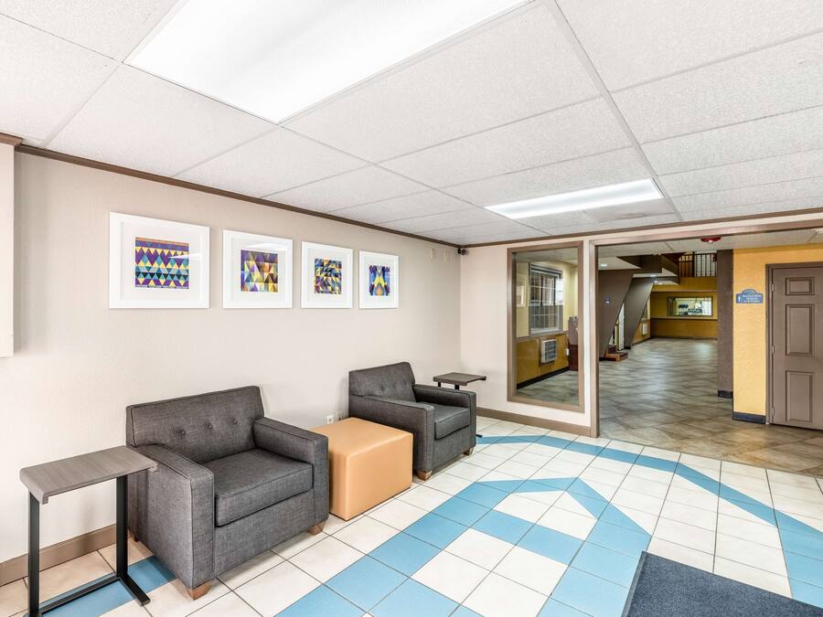 A waiting area with a sofa, armchairs, a small table, and a bench. There are framed pictures on the wall and a tiled floor.