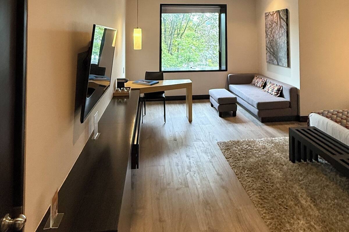 A modern living room with a large window, a flat-screen TV, a dining area, and a sofa.