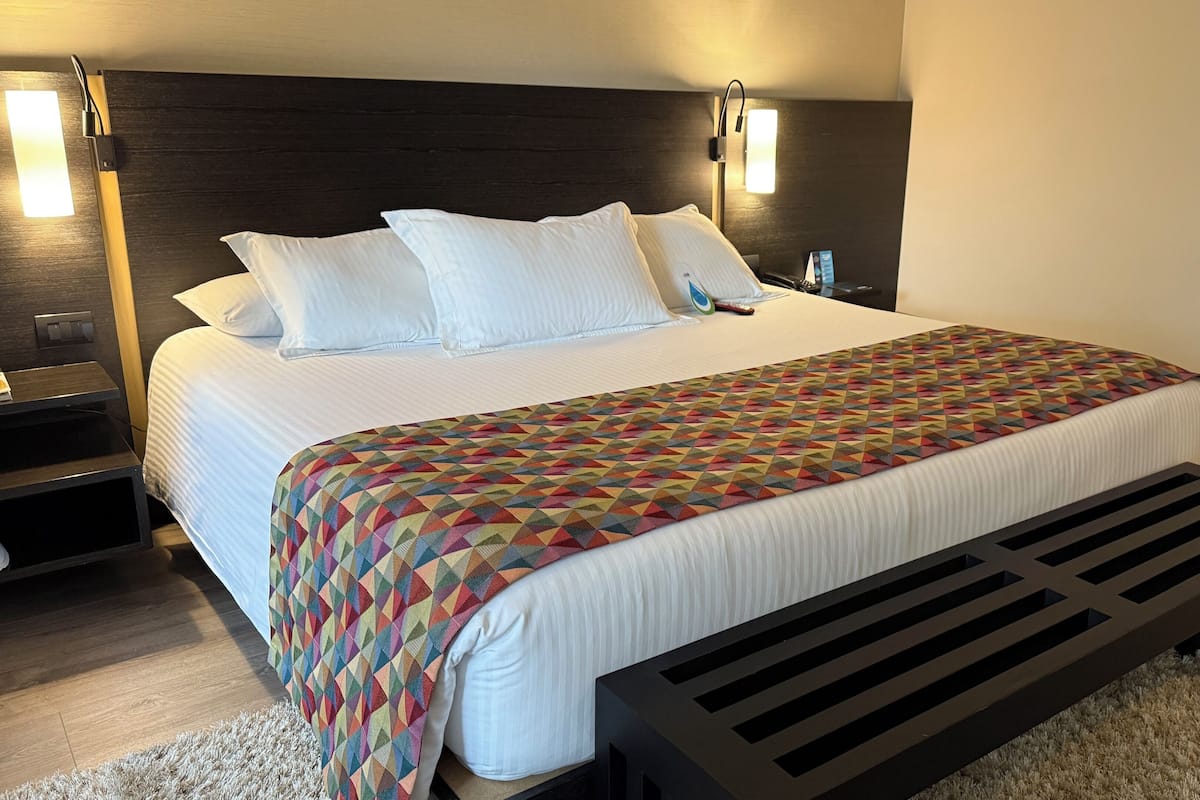 A neatly made bed with a colorful geometric-patterned blanket, a dark headboard, and bedside lamps.