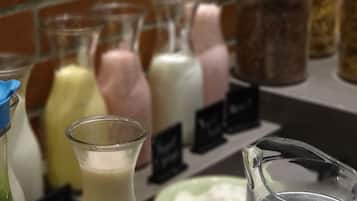 A selection of milkshakes in various flavors displayed in clear glass bottles with labels, set against a brick wall background.