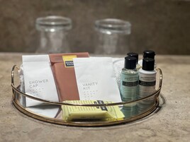 Un mobile bagno con un vassoio di vetro che contiene articoli da toilette, tra cui un berretto da doccia, un kit da toeletta e due bottiglie di shampoo e balsamo.