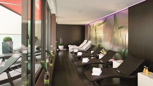 A spa area with reclining chairs, a glass wall, and a wall with a plant mural. - NH Collection Dresden Altmarkt (Dresden)