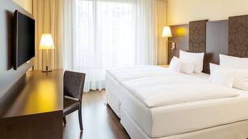 A hotel room with a bed, a desk, a chair, and a TV.