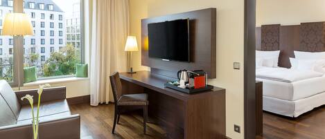 A hotel room with a desk, chair, TV, and a bed.