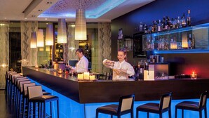 A bar area with a long counter, multiple stools, and a well-stocked bar. - NH Collection Dresden Altmarkt (Dresden)