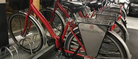 Una fila de bicicletas con cestas, con la etiqueta "NH COLLECTION", estacionadas en un garaje.