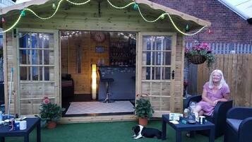 A wooden gazebo with a bar area, a dog, and a woman sitting on a chair.