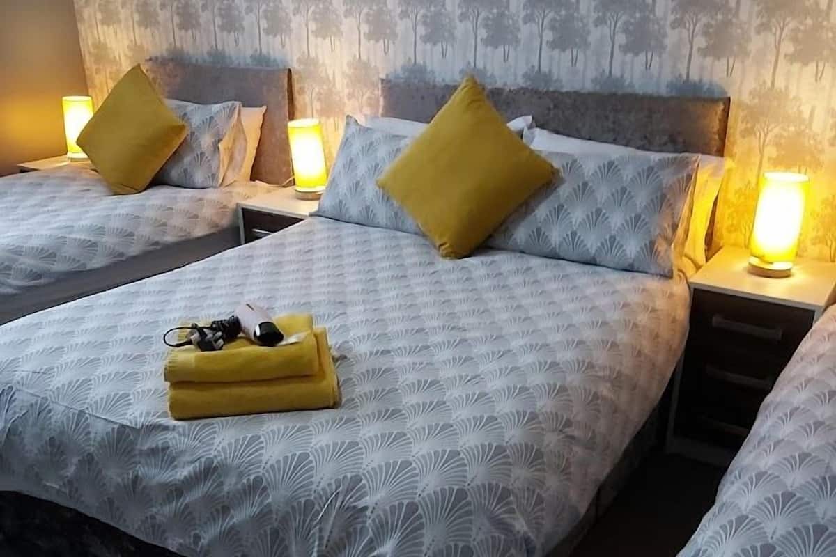 A hotel room with two beds, each with a patterned bedspread and a single yellow pillow. There are bedside lamps on each nightstand.