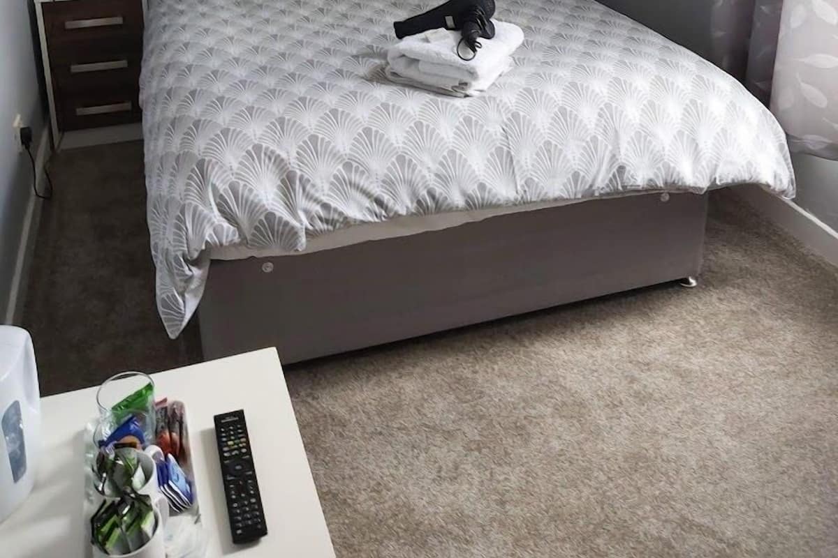 A hotel room with a large bed, a nightstand, a desk with a remote control, and a cityscape painting on the wall.