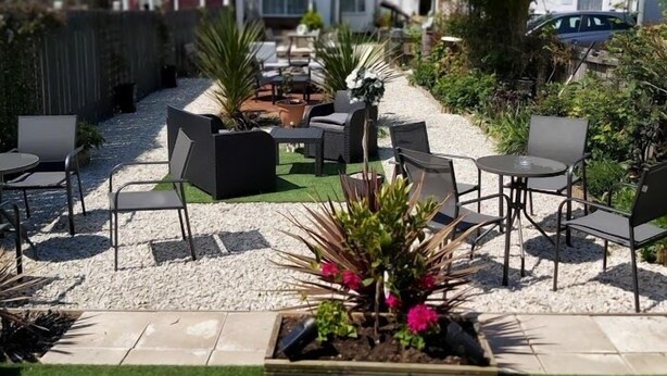 An outdoor seating area with multiple tables and chairs, surrounded by greenery and a gravel path. - The Vale Hotel (Hull)