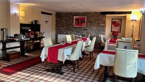 A dining area with checkered flooring, white upholstered chairs, and tables covered with red and white tablecloths. - Exmoor Manor Guest House (Lynton)