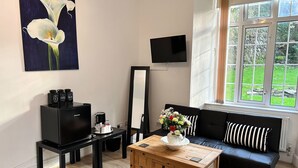 A modern living room with a wooden coffee table, a black sofa with striped cushions, a flat-screen TV mounted on the wall, a large window with a view of greenery, and a painting of white flowers on the wall. - Exmoor Manor Guest House (Lynton)