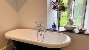 A bathroom with a freestanding bathtub, a window with a view of greenery, and a vase with flowers on the windowsill. - Exmoor Manor Guest House (Lynton)