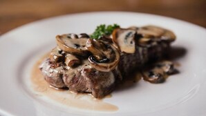 A plate with a steak topped with mushrooms and a garnish, served on a white plate. - The Silverton Inn - B&B (Exeter)