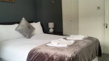 Una cama bien hecha con edredón blanco y manta marrón, una almohada y una toalla doblada sobre la cama.