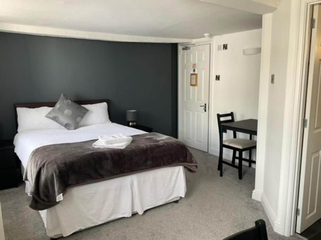 A hotel room with a bed, a chair, a desk, and a door.