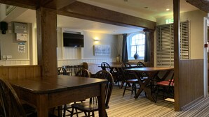 A dining area with wooden tables and chairs, a flat-screen TV mounted on the wall, and a window with blinds. - The Silverton Inn - B&B (Exeter)