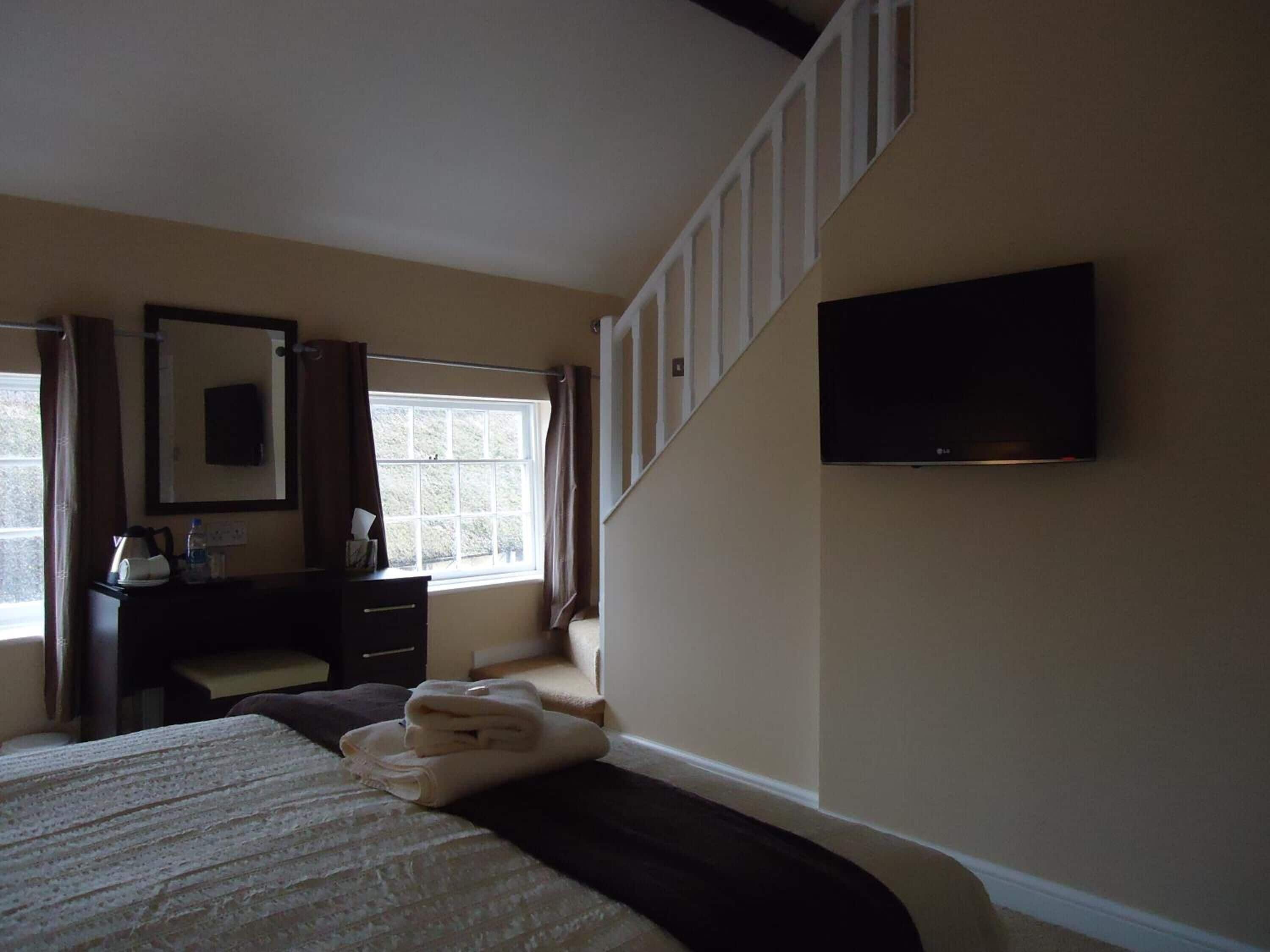 A hotel room with a bed, a dresser, a mirror, a window, and a TV mounted on the wall.