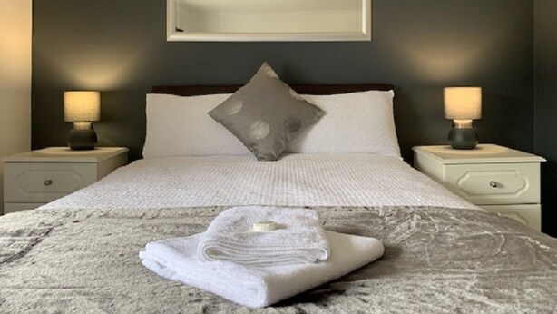 A neatly made bed with a folded towel in front, two bedside lamps, and a framed artwork above the bed. - The Silverton Inn - B&B (Exeter)