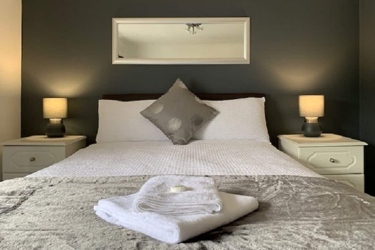 A neatly made bed with a folded towel in front, two bedside lamps, and a framed artwork above the bed.