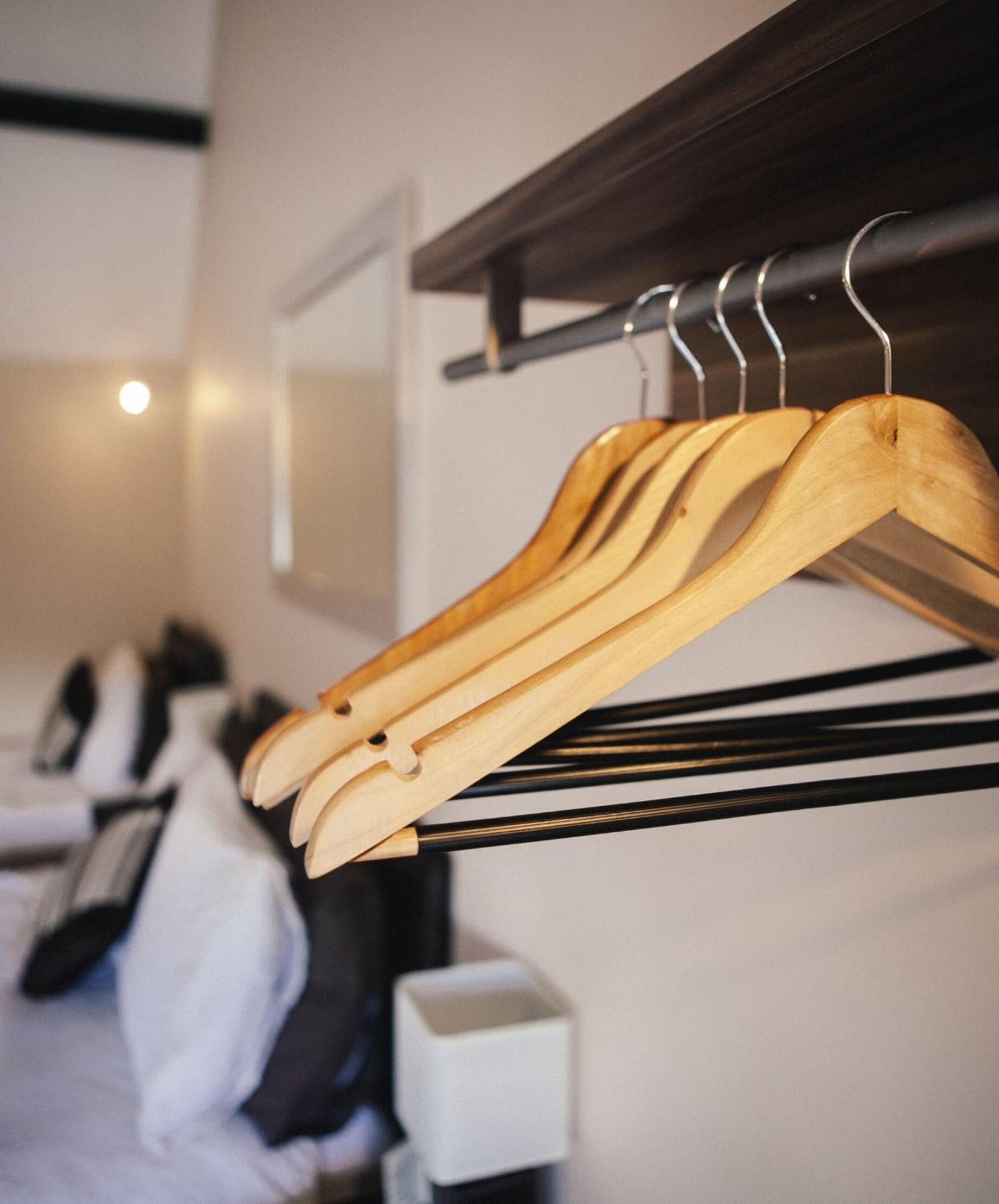 A hotel room with a wooden hanger rack holding multiple hangers, a bed with white bedding, and a small white box on the floor.