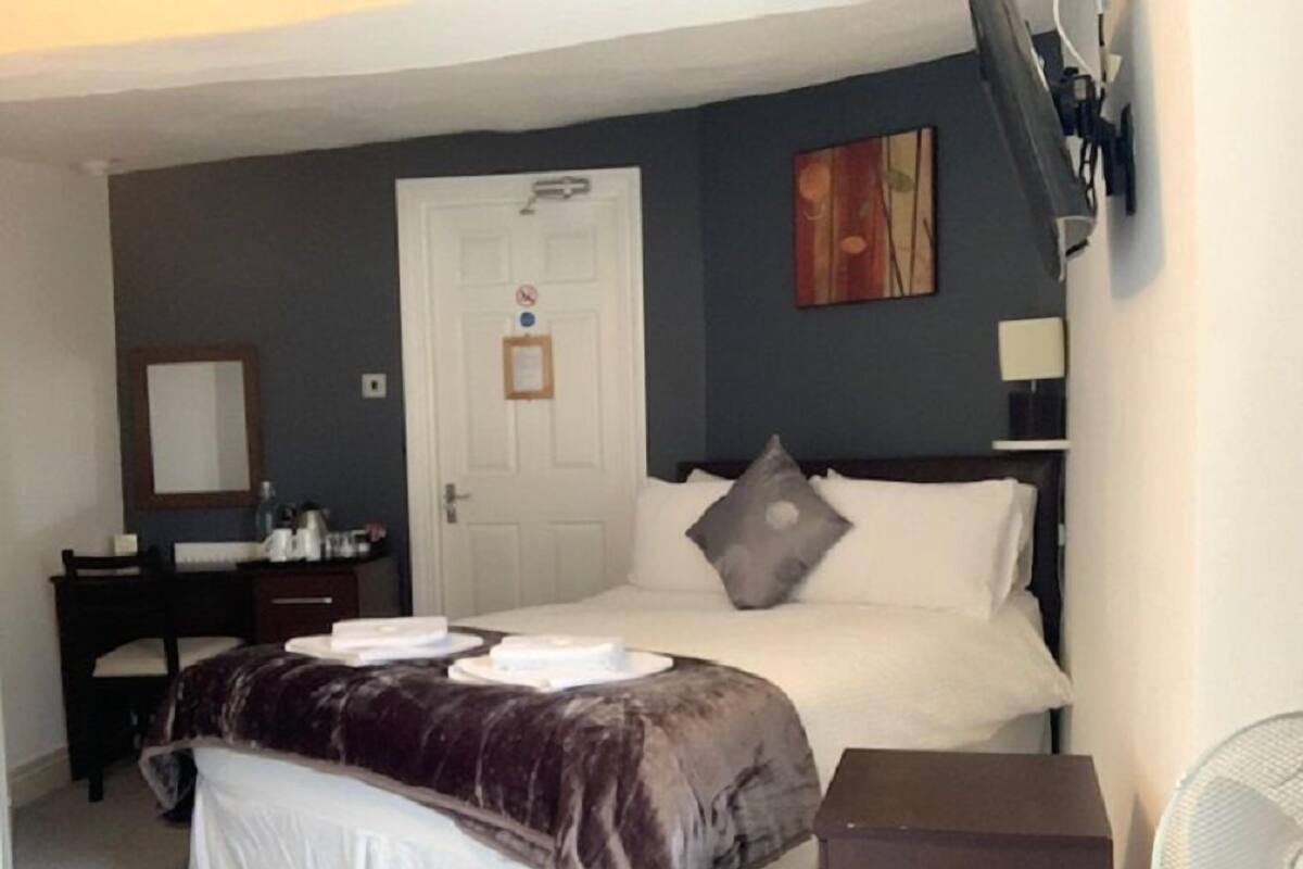 A bedroom with a bed, a dresser, a desk, a mirror, and a door.