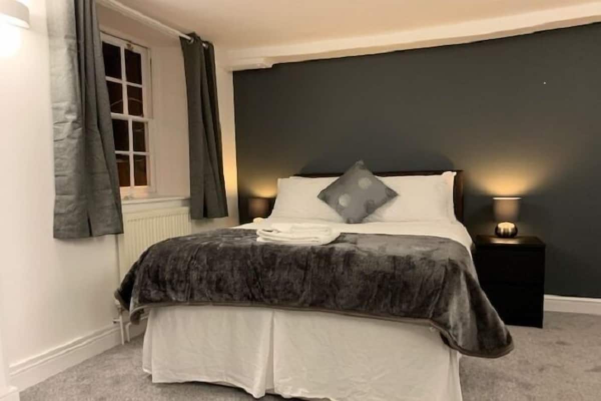 A bedroom with a bed, a nightstand, a lamp, and a window with curtains.