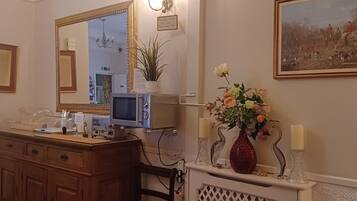 A hotel room with a wooden dresser, a chair, a mirror, a television, a fireplace with a lattice front, and a painting on the wall.