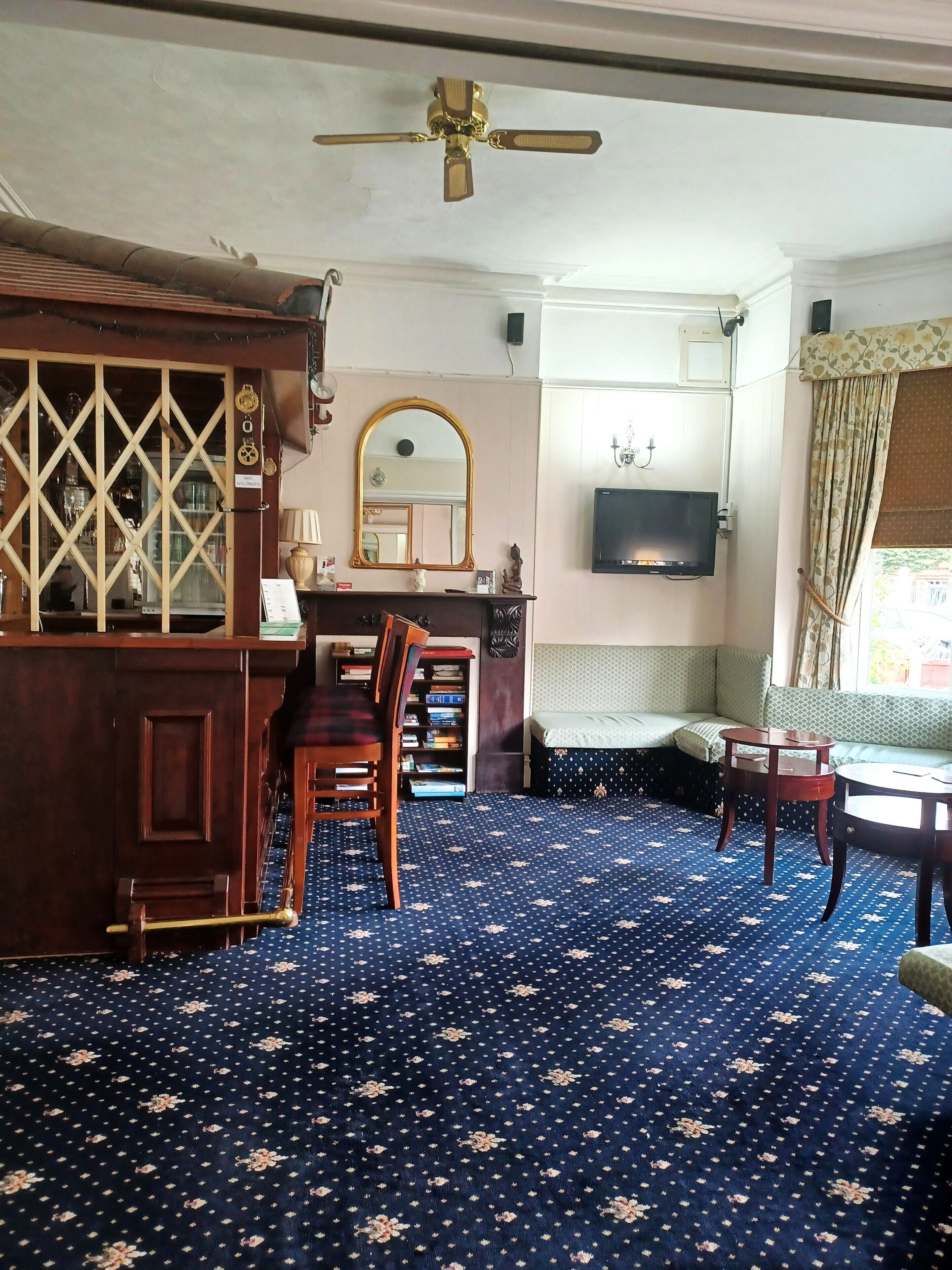 A room with a ceiling fan, a TV mounted on the wall, a sofa, a wooden cabinet, and a patterned carpet.