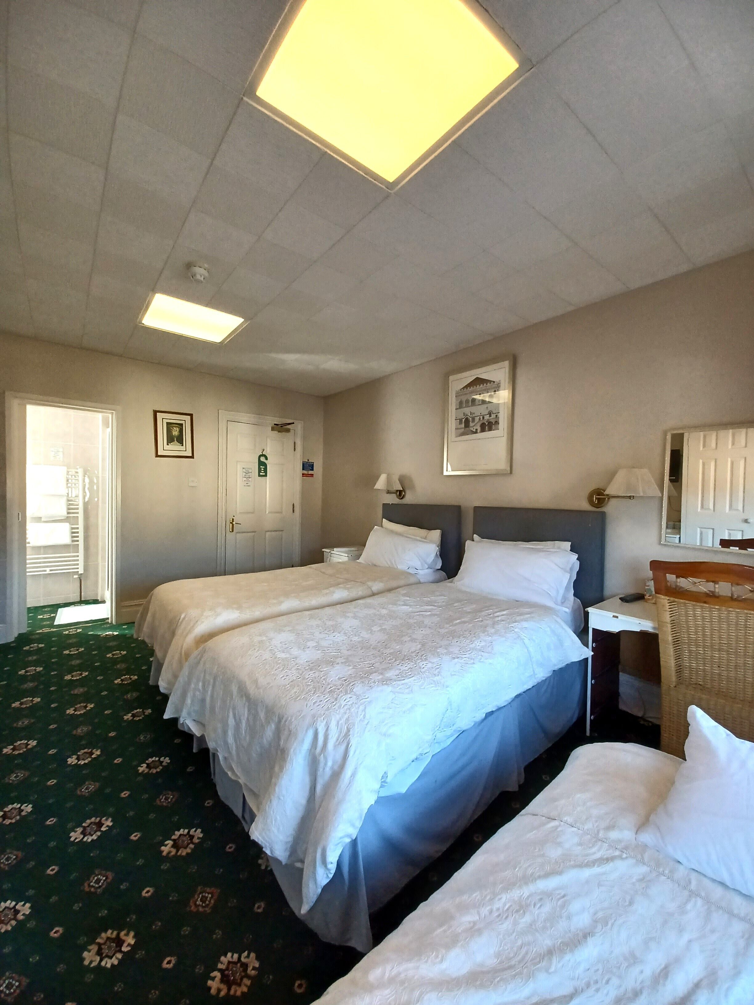 A hotel room with two beds, a desk, a chair, a lamp, and a framed picture on the wall.