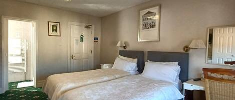 A hotel room with two beds, a desk, a chair, a lamp, and a framed picture on the wall.