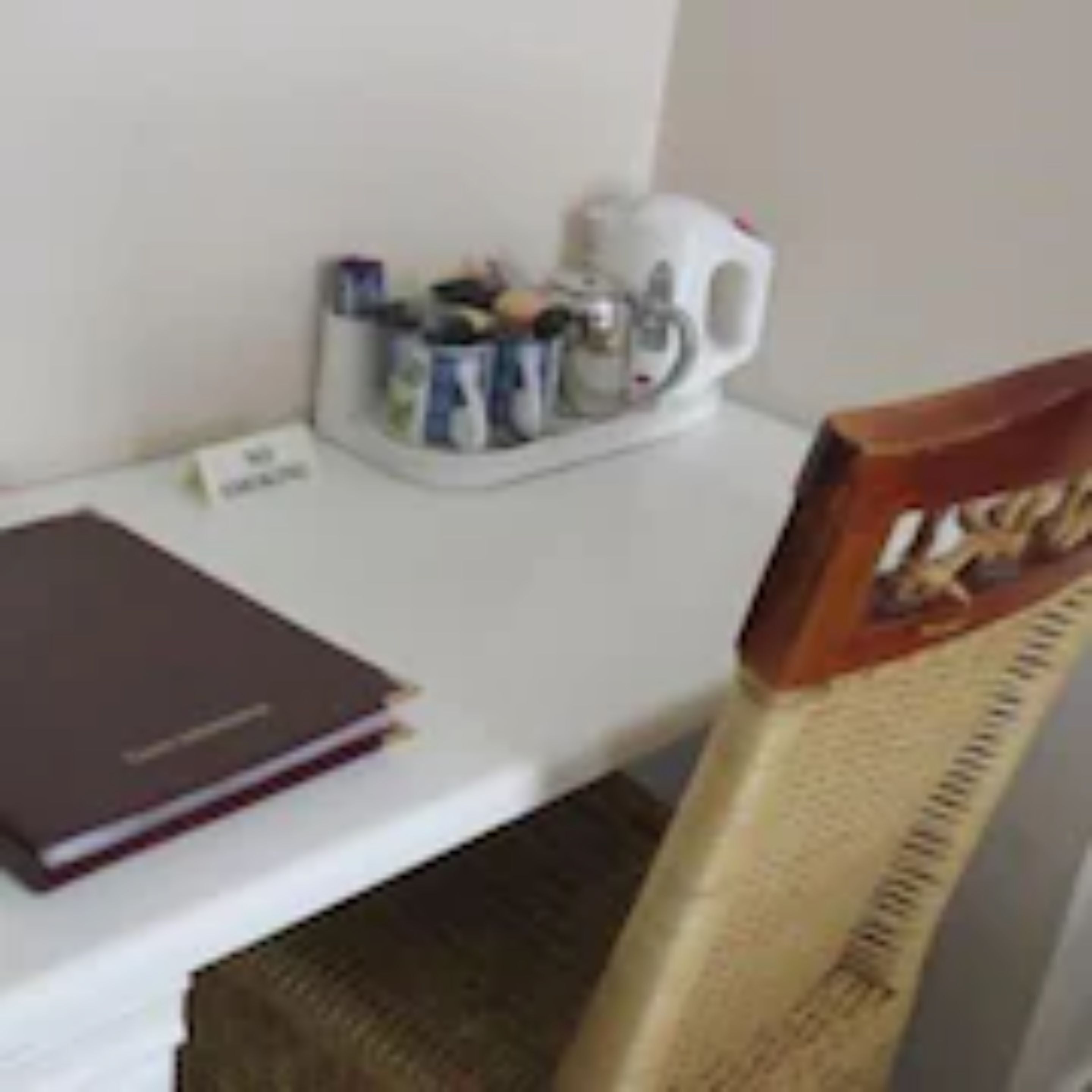 Un pequeño escritorio blanco con una libreta, una taza y un portavasos con diversos objetos.