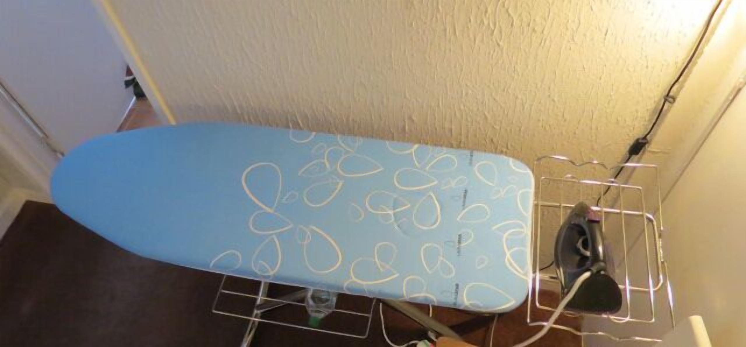 Una tabla de planchar con superficie azul y una rejilla metálica que sostiene un planchador.