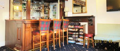 A bar area with wooden bar counter and chairs, a bookshelf with books, and a mirror on the wall.