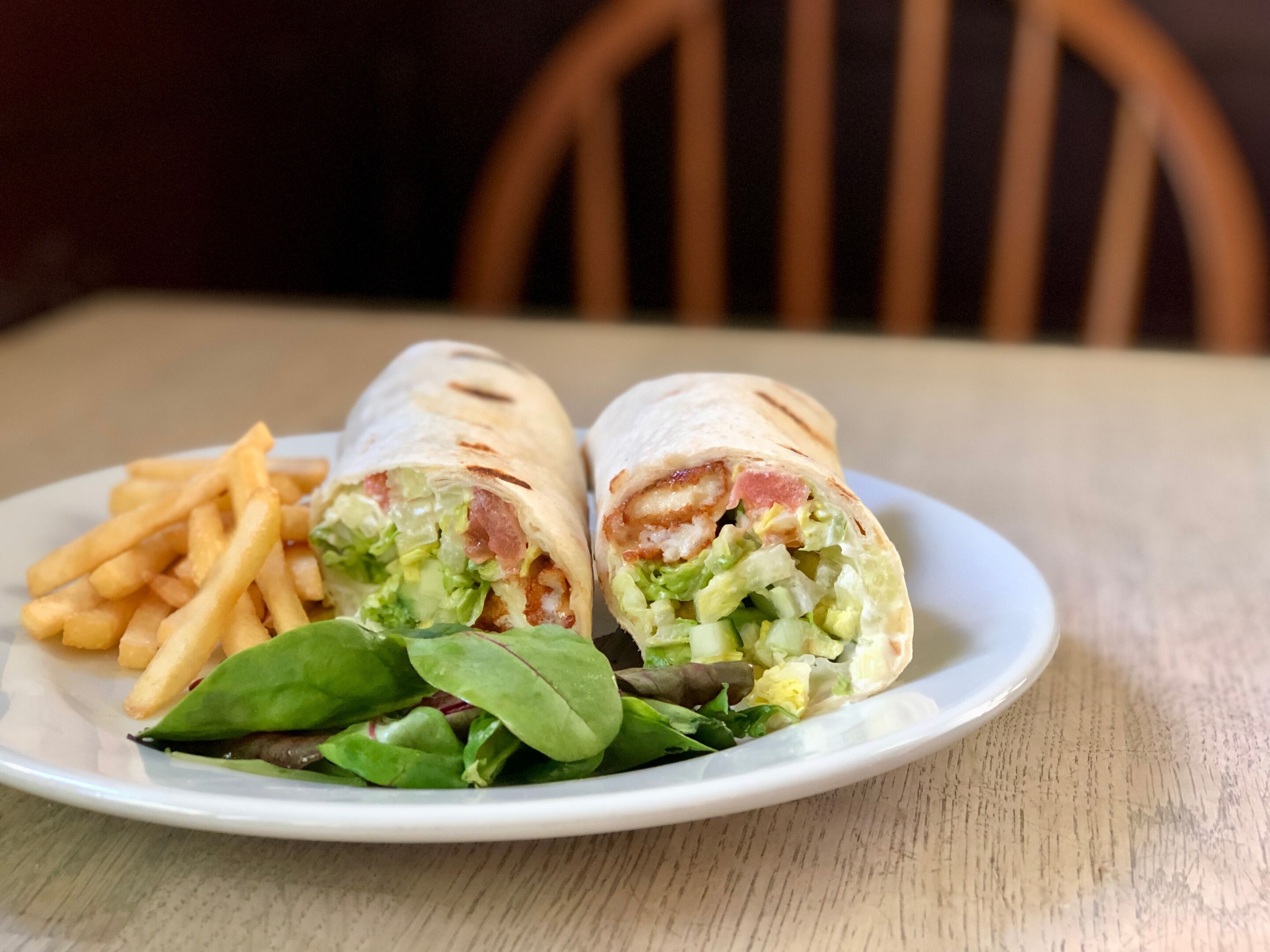Un plato con un wrap, papas fritas y vegetales verdes.