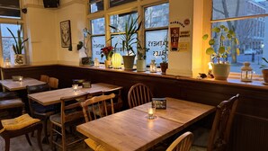 Un restaurante acogedor con mesas y sillas de madera, plantas en macetas en el alféizar de la ventana, y un cartel que anuncia un pub cada lunes.