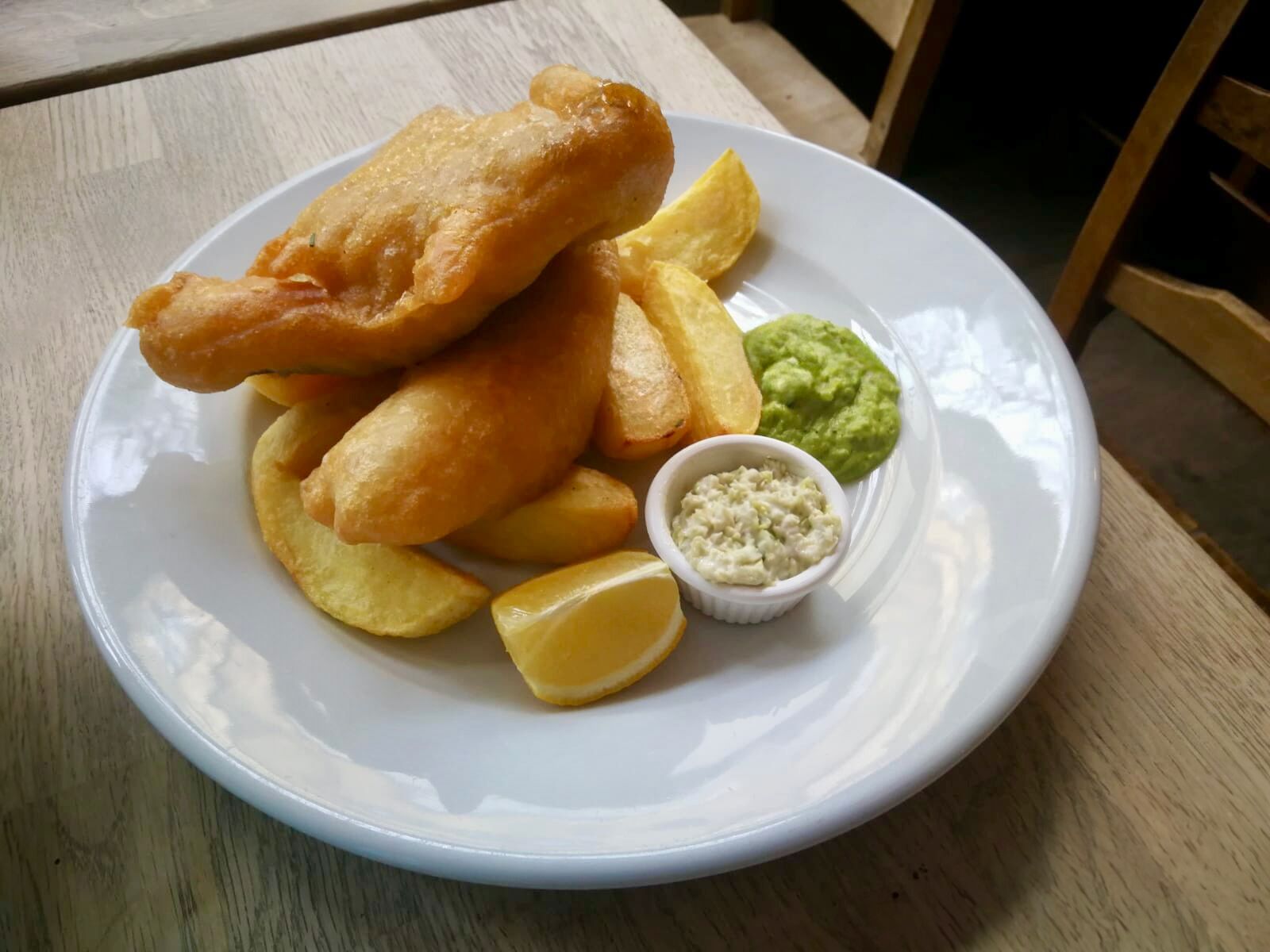 Une assiette de poisson-frites accompagnée de quartiers de pommes de terre, de purée de petits pois et de sauce tartare.