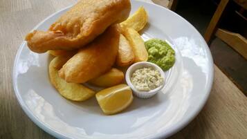 Une assiette de poisson-frites accompagnée de quartiers de pommes de terre, de purée de petits pois et de sauce tartare.